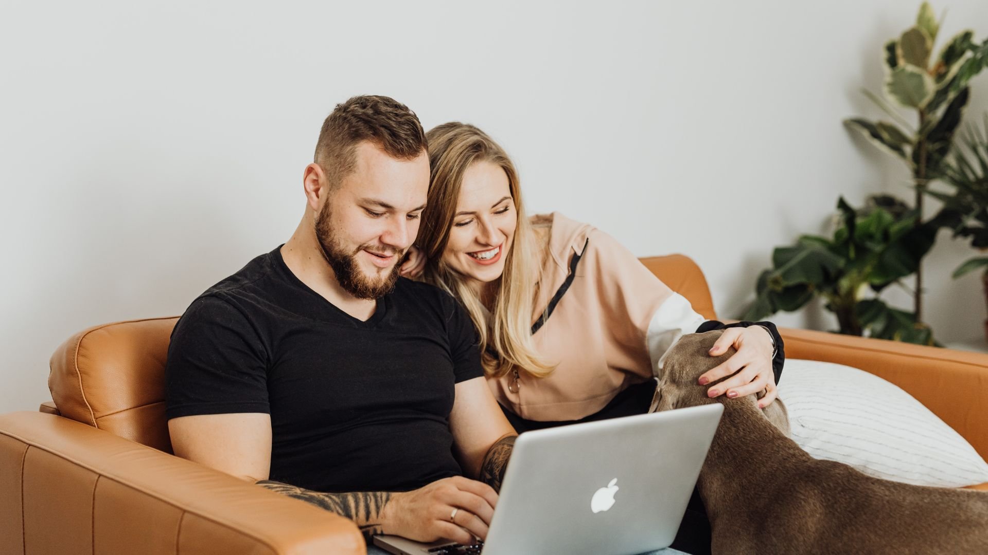 Two people sitting with their dog looking at a laptop